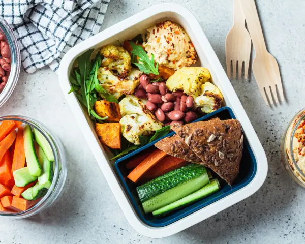 Un repas tiré du sac sain et coloré : houmous, légumes rôtis, haricots rouges, pain complet et crudités. Parfait pour un déjeuner sur le pouce.