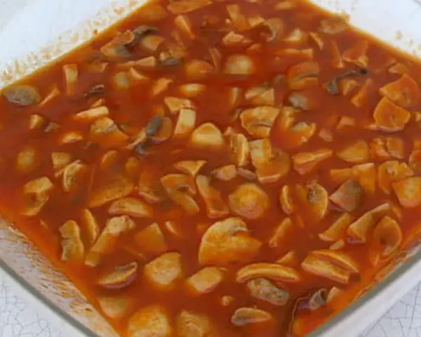 Champignons à la grecque, une préparation savoureuse de champignons coupés en morceaux, mijotant dans une sauce tomate riche et parfumée.