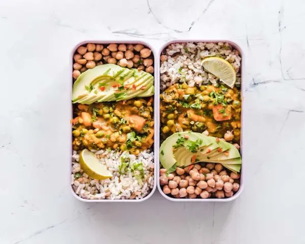Deux lunch box remplies d'une idée lunch box école saine : curry de légumes, riz, pois chiches et avocat.