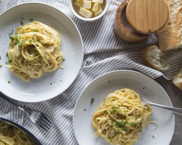 Deux assiettes de pâtes crémeuses à l'ail, garnies de persil frais. Un pain croustillant et du fromage râpé complètent cette recette de pâtes à l'ail et crème.