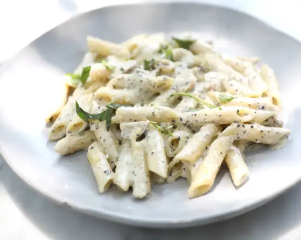 Pâtes penne nappées d'une sauce crémeuse à l'ail, parsemées de fines herbes fraîches, servies sur une assiette blanche.