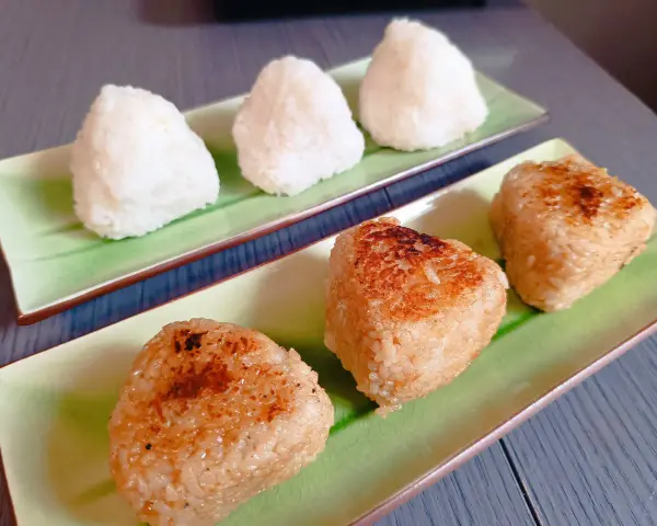 Sur des assiettes vertes, des onigiris nature et grillés, parfaits pour un pique-nique japonais.