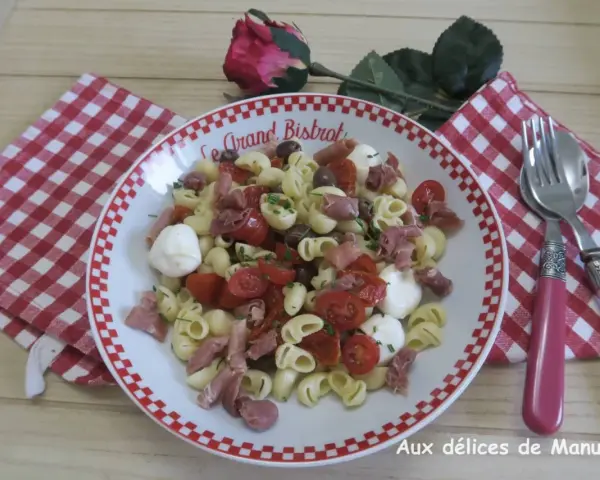 Une savoureuse salade italienne de pâtes avec tomates cerises, mozzarella, olives et jambon cru, garnie de ciboulette.
