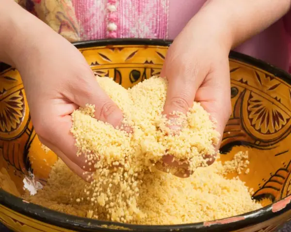 Mains travaillant du couscous marocain dans un plat traditionnel décoré.