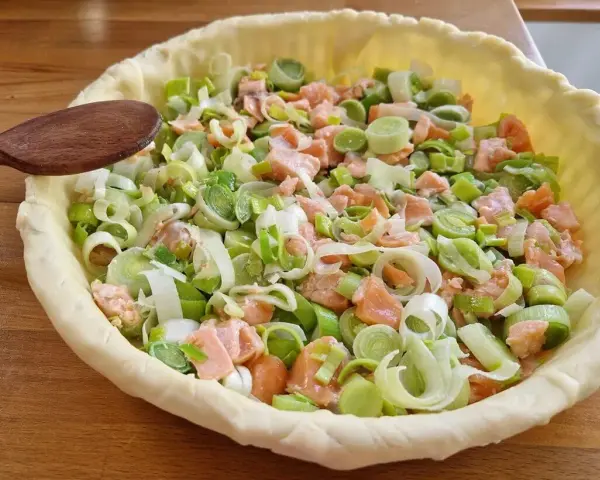 Préparation d'un plat végétarien : une tarte garnie de saumon et de poireaux coupés, prête à être cuite.