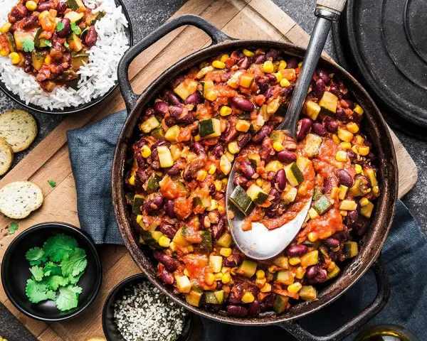Un plat de chili végétarien copieux avec des haricots rouges, du maïs et des courgettes, servi avec du riz blanc.