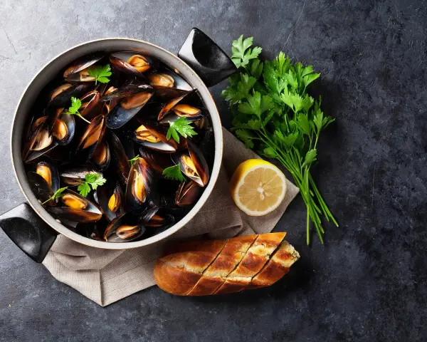 Un plat de moules au rosé, garni de persil frais, avec un quartier de citron et une baguette à l'ail.