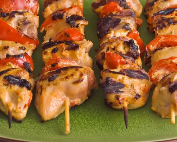 Brochettes de poulet grillé avec poivrons rouges sur une assiette verte. Parfait pour savoir quoi servir avec des brochettes de poulet.