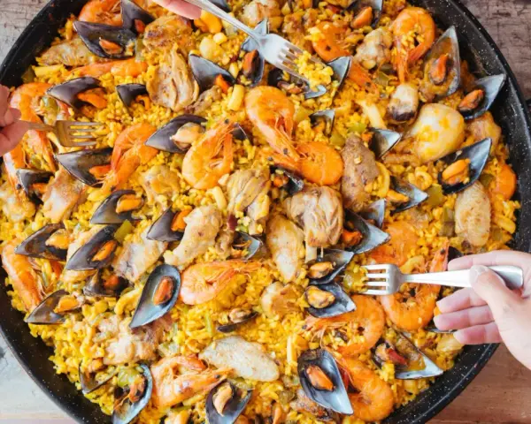 Un plat généreux de poulet paella, garni de crevettes et de moules, prêt à être dégusté par plusieurs mains.