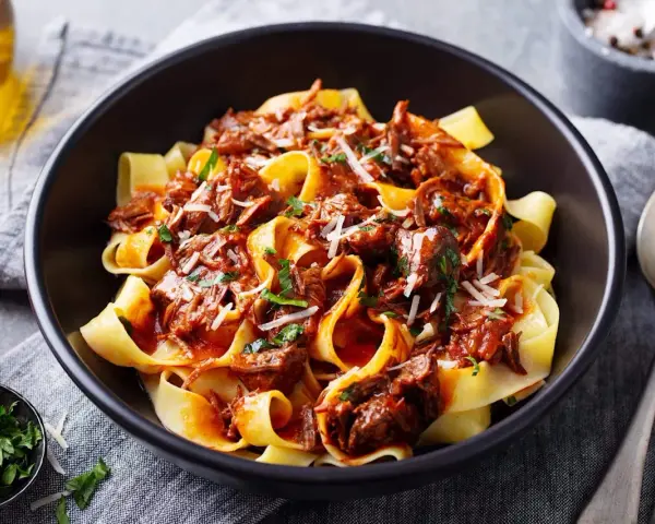 Pâtes larges nappées d'une riche sauce à la palette de boeuf effilochée, parsemées de parmesan et de persil frais.