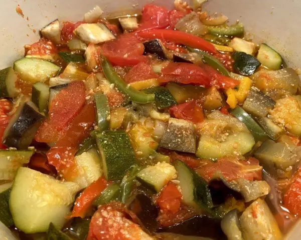 Un plat coloré de ratatouille niçoise, avec des morceaux de courgettes, aubergines, tomates et poivrons mijotés.