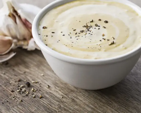 Sauce césar sans oeuf crémeuse, parsemée de poivre noir, avec une tête d'ail en arrière-plan sur fond de bois.
