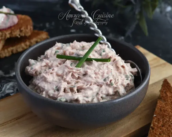 Un bol de rillettes de thon crémeuses, garni de ciboule, prêt à être tartiné sur des toasts grillés.