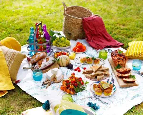 Un pique-nique gourmand sur l'herbe : pains, fromages, fruits, mini quiches, sandwichs, roulé salé, et boissons colorées. Une belle idée pique-nique !