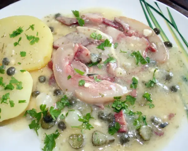 Tête de veau en sauce avec des pommes de terre et des câpres, garnie de persil frais.