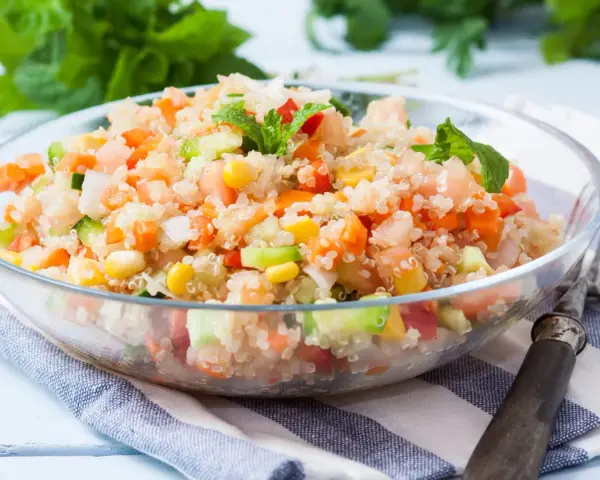 Salade quinoa colorée avec des dés de tomates, carottes, concombre et maïs, garnie de feuilles de menthe fraîche.