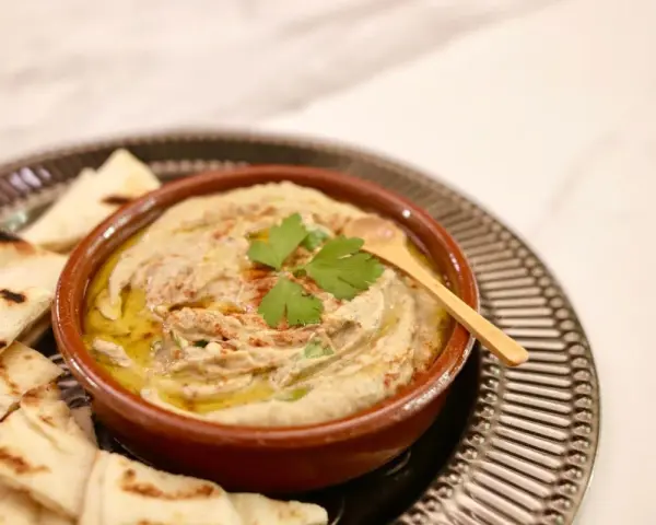Un bol de baba ganoush crémeux, garni de persil frais et d'un filet d'huile d'olive, servi avec des pains pita grillés.