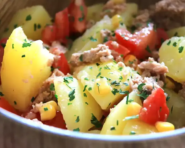 Salade de pommes de terre, thon, tomates et maïs, garnie de persil frais. Un plat simple et savoureux.