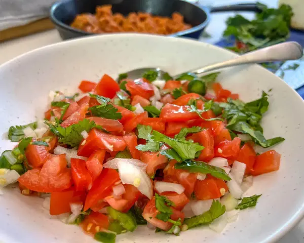 Un bol de pico de gallo frais, garni de coriandre, prêt à être dégusté.