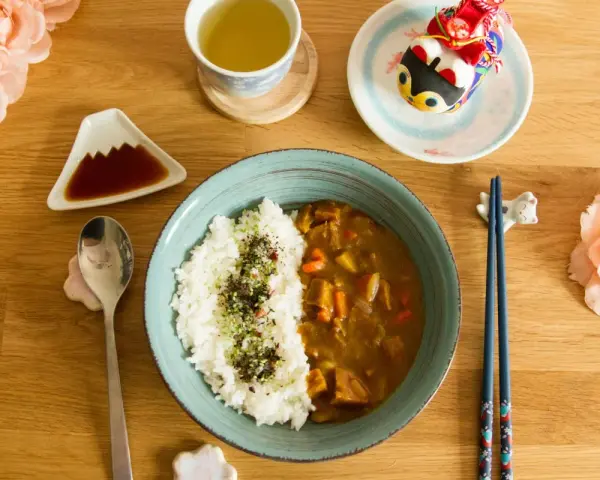 Un délicieux curry japonais avec du riz blanc, servi avec une tasse de thé et des décorations mignonnes.