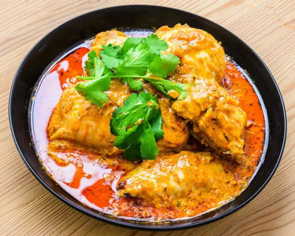 Un plat de poulet vindaloo, un curry indien épicé, servi dans un bol noir avec de la coriandre fraîche.
