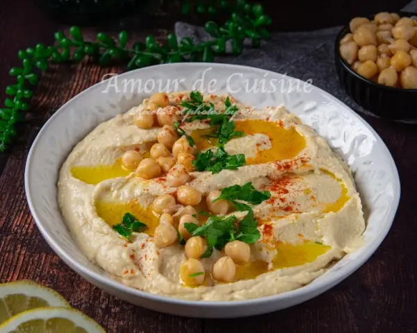 Un plat de houmous crémeux, garni de pois chiches, persil et paprika. Parfait pour découvrir 7 recettes de houmous maison.