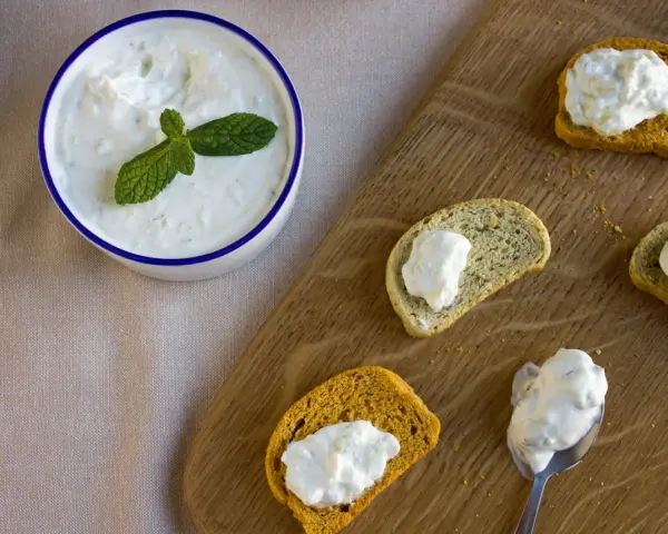 Un bol de crème tzatziki frais, garni de menthe, est servi avec des toasts.