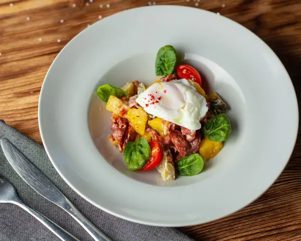 Salade colorée avec œuf poché, tomates cerises, lardons et quelques feuilles de salade légumes verts.