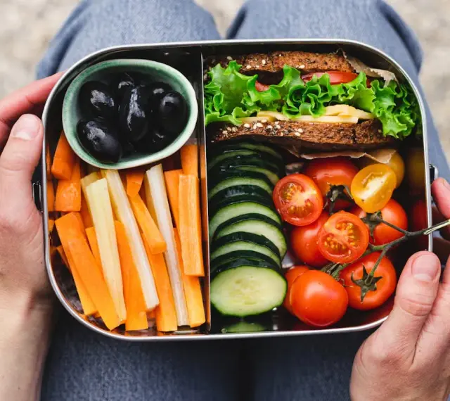 Un bento sain avec sandwich, bâtonnets de carottes et céleri, tomates cerises, concombres et olives noires.
