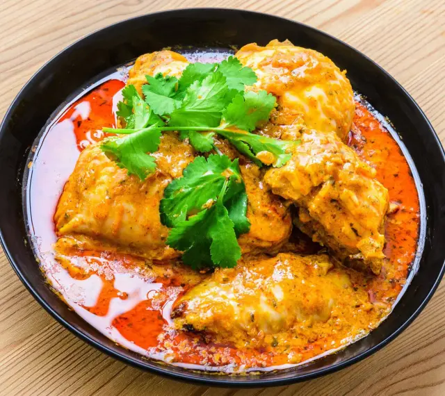 Un plat de poulet vindaloo, un curry indien épicé, servi dans un bol noir avec de la coriandre fraîche.