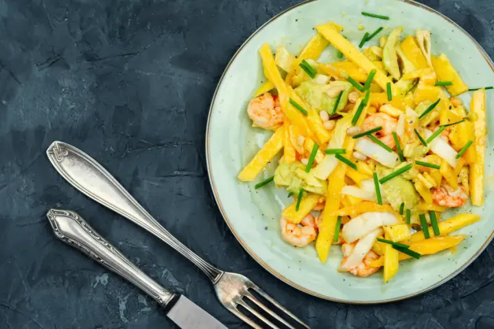 Salade colorée avec des crevettes, de l'avocat et des bâtonnets de mangue, garnie de ciboule. Un délice frais et fruité.