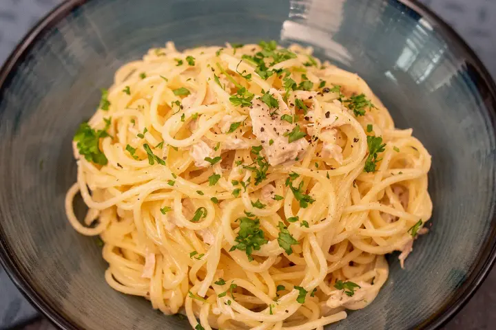 Un plat de pâtes au thon, garni de persil frais et de poivre noir, servi dans un bol bleu.