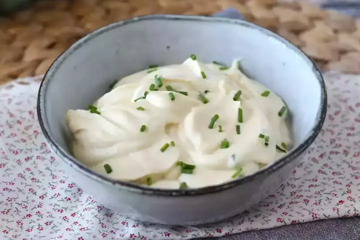 Mayonnaise sans huile crémeuse, garnie de ciboulette fraîche, dans un bol en céramique. Parfait pour un repas léger.