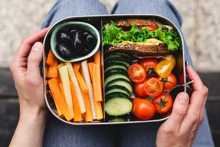 Un bento sain avec sandwich, bâtonnets de carottes et céleri, tomates cerises, concombres et olives noires.