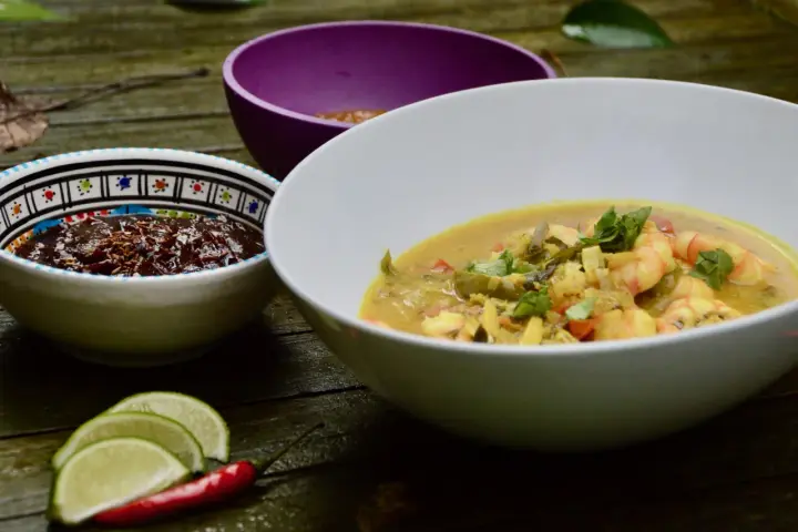 Un plat de crevette curry coco crémeux, garni de coriandre fraîche, servi avec des quartiers de citron vert et un piment rouge.