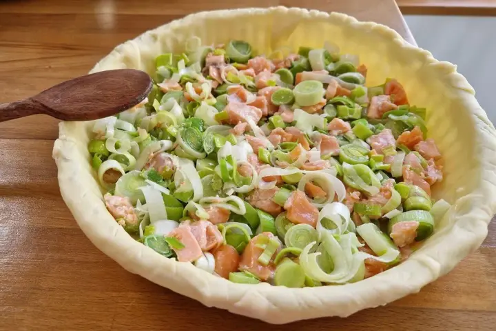 Préparation d'un plat végétarien : une tarte garnie de saumon et de poireaux coupés, prête à être cuite.