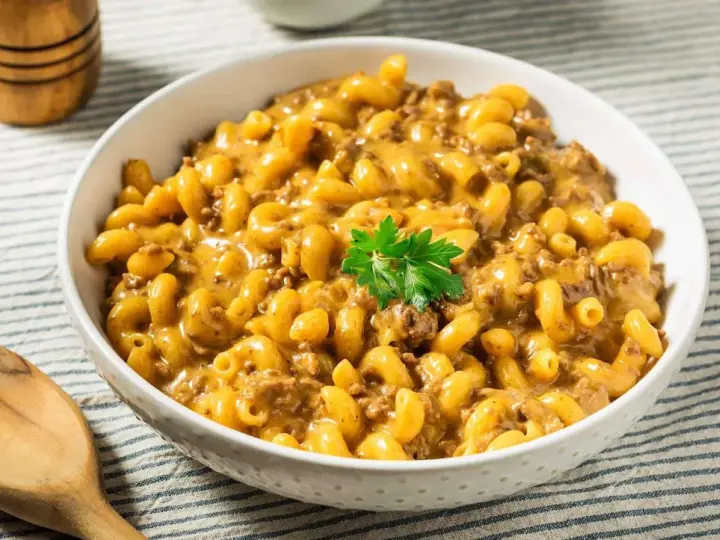 Un bol de macaroni au fromage crémeux avec du bœuf haché, garni de persil. Un plat parfait pour un dîner rapide et facile.