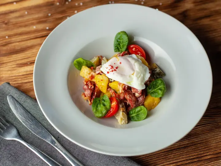 Salade colorée avec œuf poché, tomates cerises, lardons et quelques feuilles de salade légumes verts.