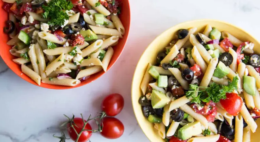 Deux bols de salade de pâtes méditerranéenne colorée, garnie de feta, olives, tomates et avocat.