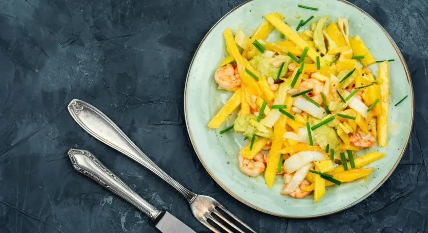 Salade colorée avec des crevettes, de l'avocat et des bâtonnets de mangue, garnie de ciboule. Un délice frais et fruité.