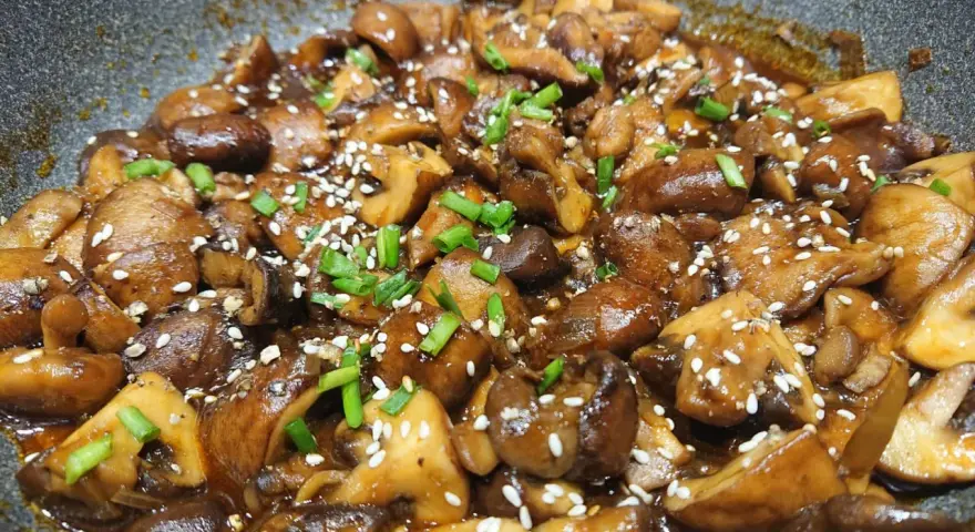Champignons caramélisés chinois, brillants et appétissants, saupoudrés de graines de sésame et de ciboule fraîche.