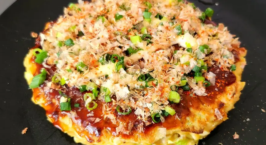 Un délicieux okonomiyaki, un plat emblématique du repas japonais maison, garni d'oignons verts et de flocons de bonite.