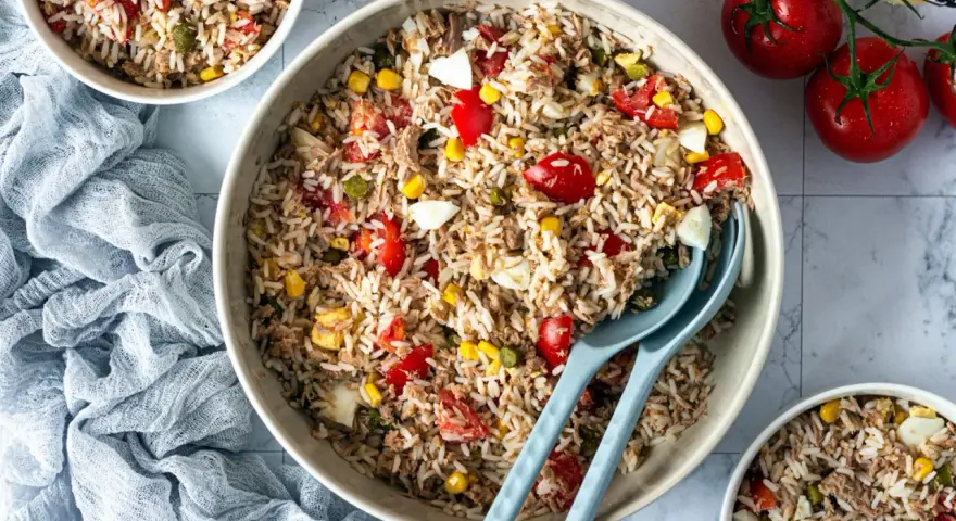 Un grand bol de salade de riz thon, garnie de tomates, maïs et œufs durs. Parfait pour un repas frais et léger.