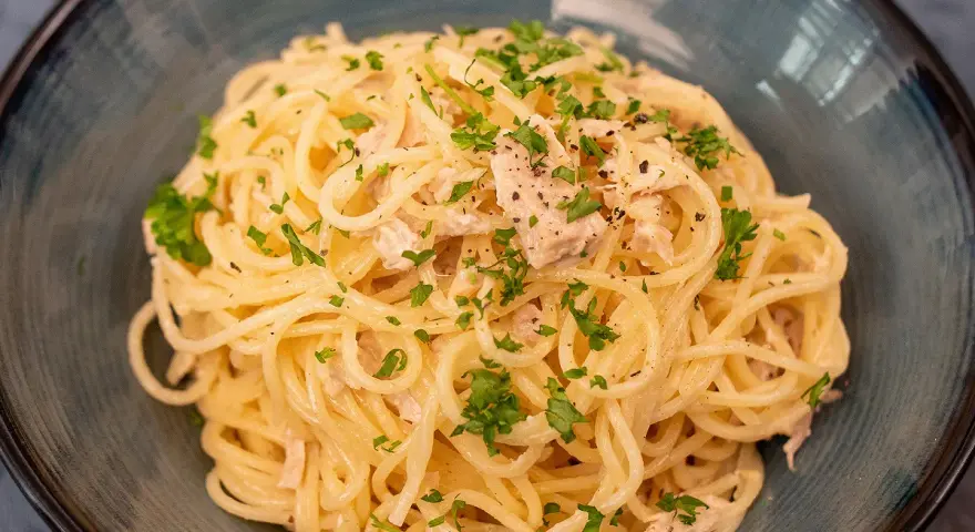Un plat de pâtes au thon, garni de persil frais et de poivre noir, servi dans un bol bleu.
