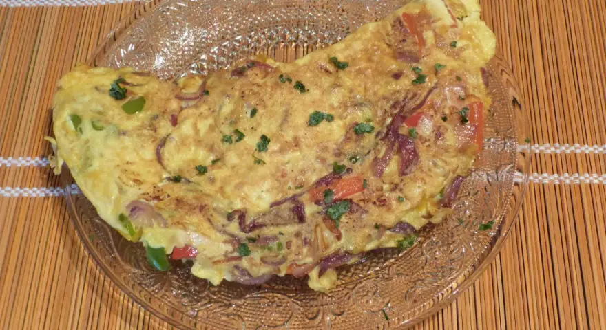 Une savoureuse omelette mexicaine garnie d'oignons rouges, de poivrons et d'herbes fraîches, servie sur une assiette en verre.