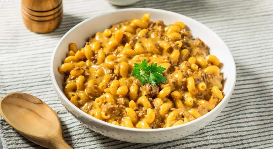 Un bol de macaroni au fromage crémeux avec du bœuf haché, garni de persil. Un plat parfait pour un dîner rapide et facile.