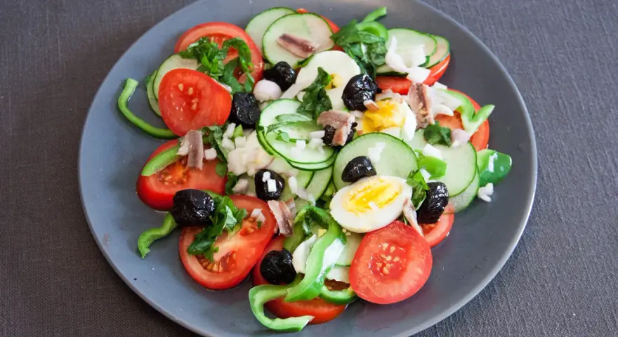 Salade niçoise colorée avec tomates, concombres, œufs, olives noires et anchois.