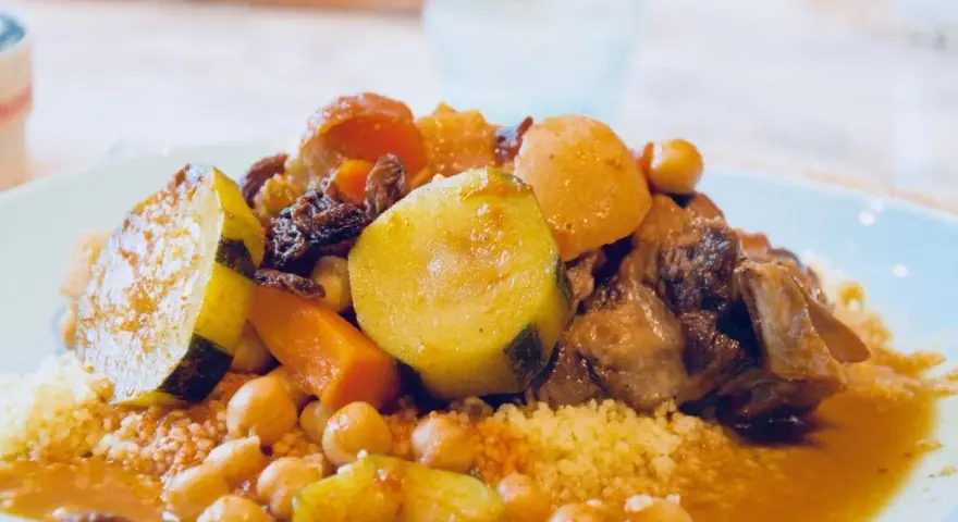Un plat généreux de couscous algérien avec légumes, pois chiches, raisins secs et viande mijotée dans une sauce savoureuse.