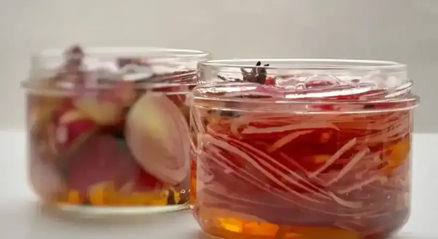 Deux bocaux de pickles d'oignon rouge, l'un avec des oignons entiers, l'autre avec des lamelles fines, baignant dans une marinade ambrée.