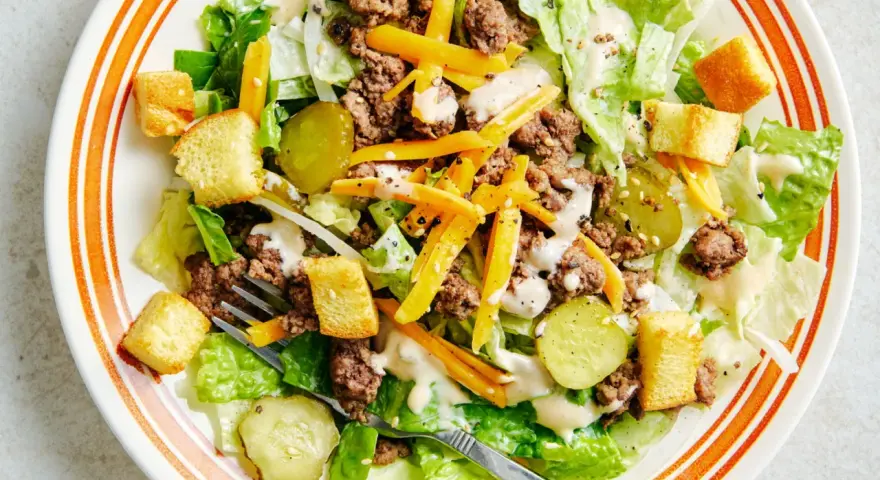Salade Big Mac avec laitue, bœuf haché, fromage râpé, croûtons et cornichons, arrosée d'une sauce crémeuse.